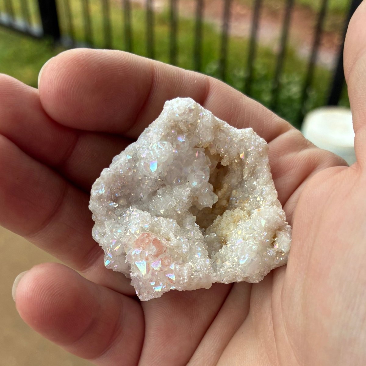 White aura coated quartz geode in a palm of a hand, in natural outdoor lighting.